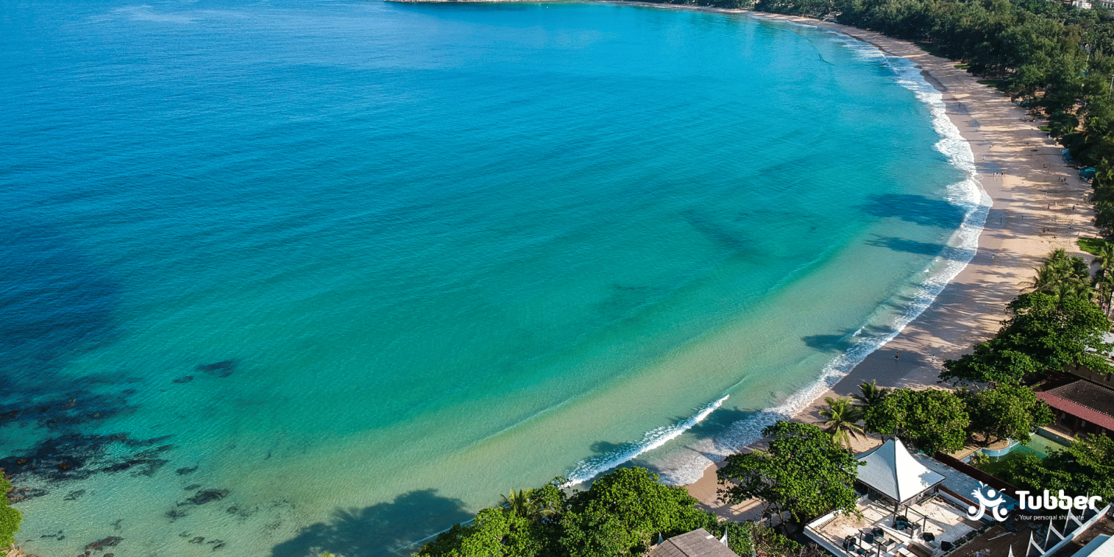 Aerial view of Kata Beach on Phukets west coast with gentle waves, wide golden sands, and tropical tree-lined shoreline