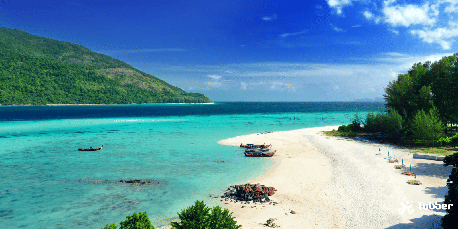 Scenic view of Koh Lipes beach with longtail boats and turquoise shallows, backed by green hills and quiet island atmosphere