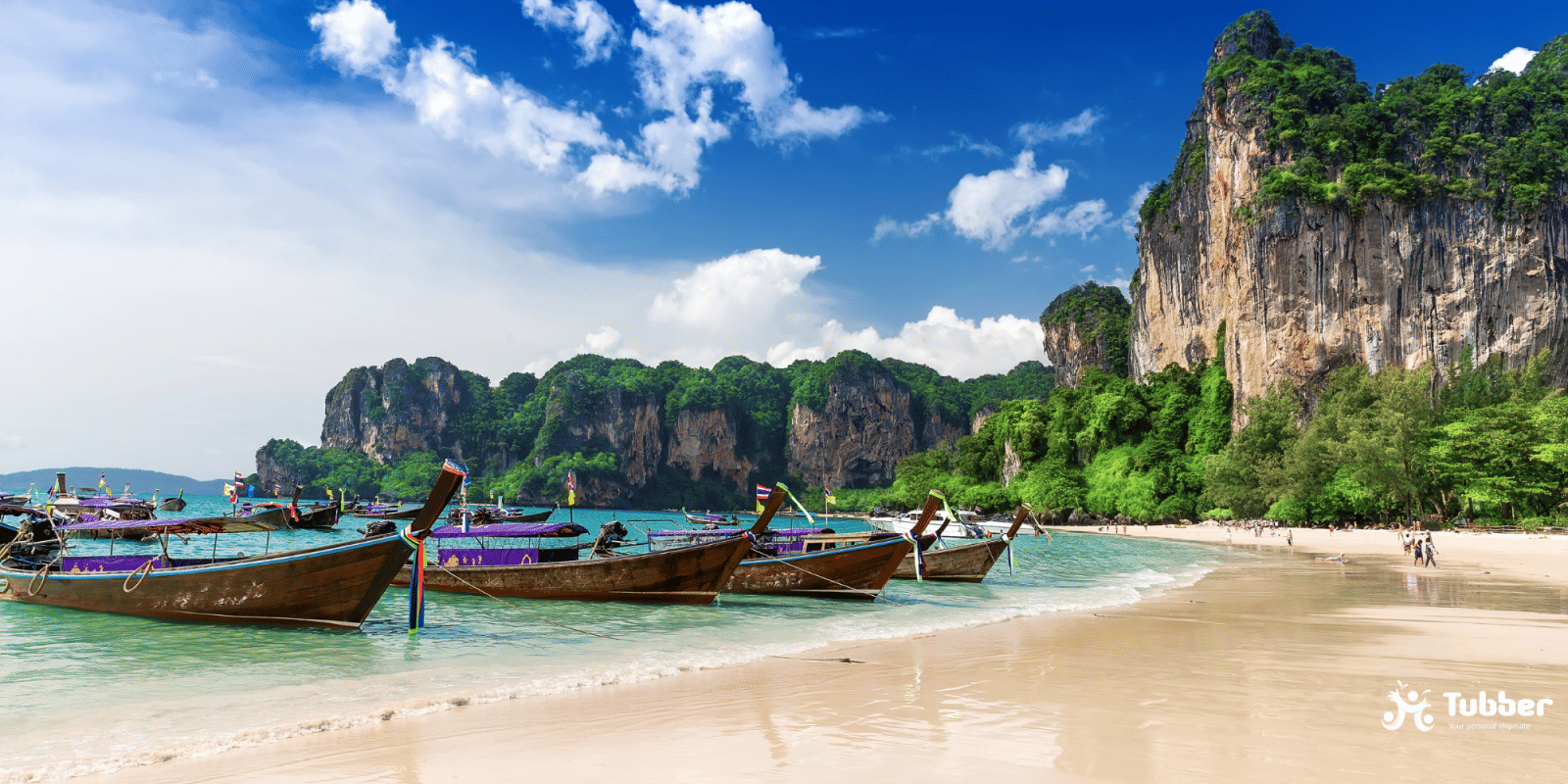 Longtail boats resting along Railay Beach with towering limestone cliffs and clear blue skies in Krabi, Thailand