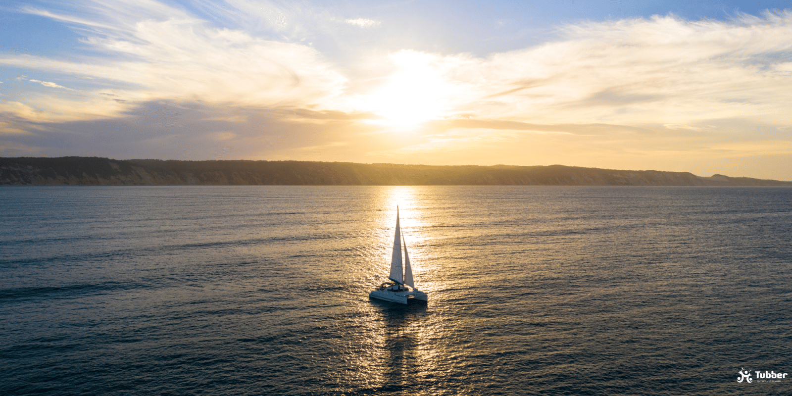 Catamaran sailing at sunset in Thailand, peaceful ocean view, golden sky, and coastal cliffs in the distance