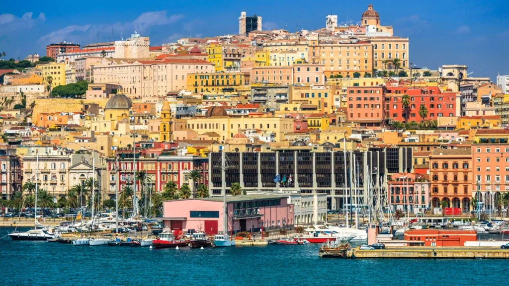 Um cais em Cagliari, na Sardenha, com muitos barcos e casas coloridas ao fundo.